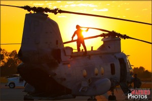 The setting sun shines behind a crew member preparing a CH-46E Sea Knight