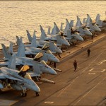 A row of F/A-18C Hornets from various squadrons sit on the forward deck of the USS Abraham Lincoln Aircraft Carrier