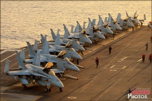 A row of F/A-18C Hornets from various squadrons sit on the forward deck of the USS Abraham Lincoln Aircraft Carrier